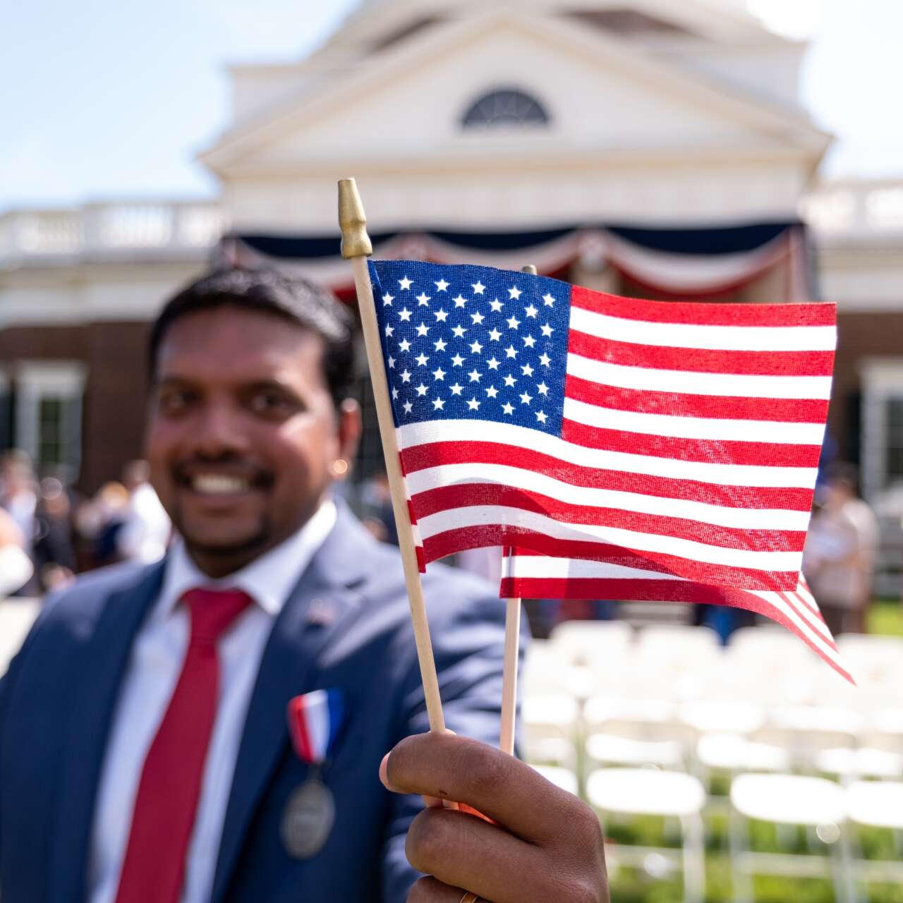 A man stands in front of a building, smiling and posing for a photo while holding the U.S. flag.