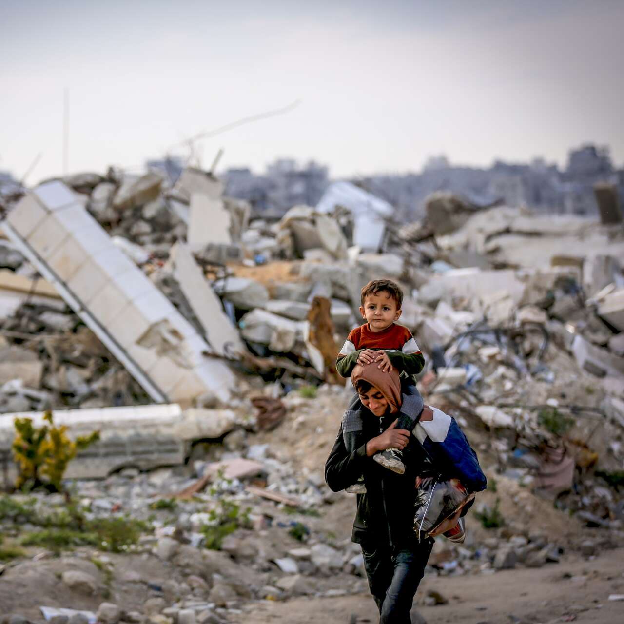 폭격으로 폐허가 된 거리를 한 아버지가 아이를 등에 업고 탈출하고 있습니다.