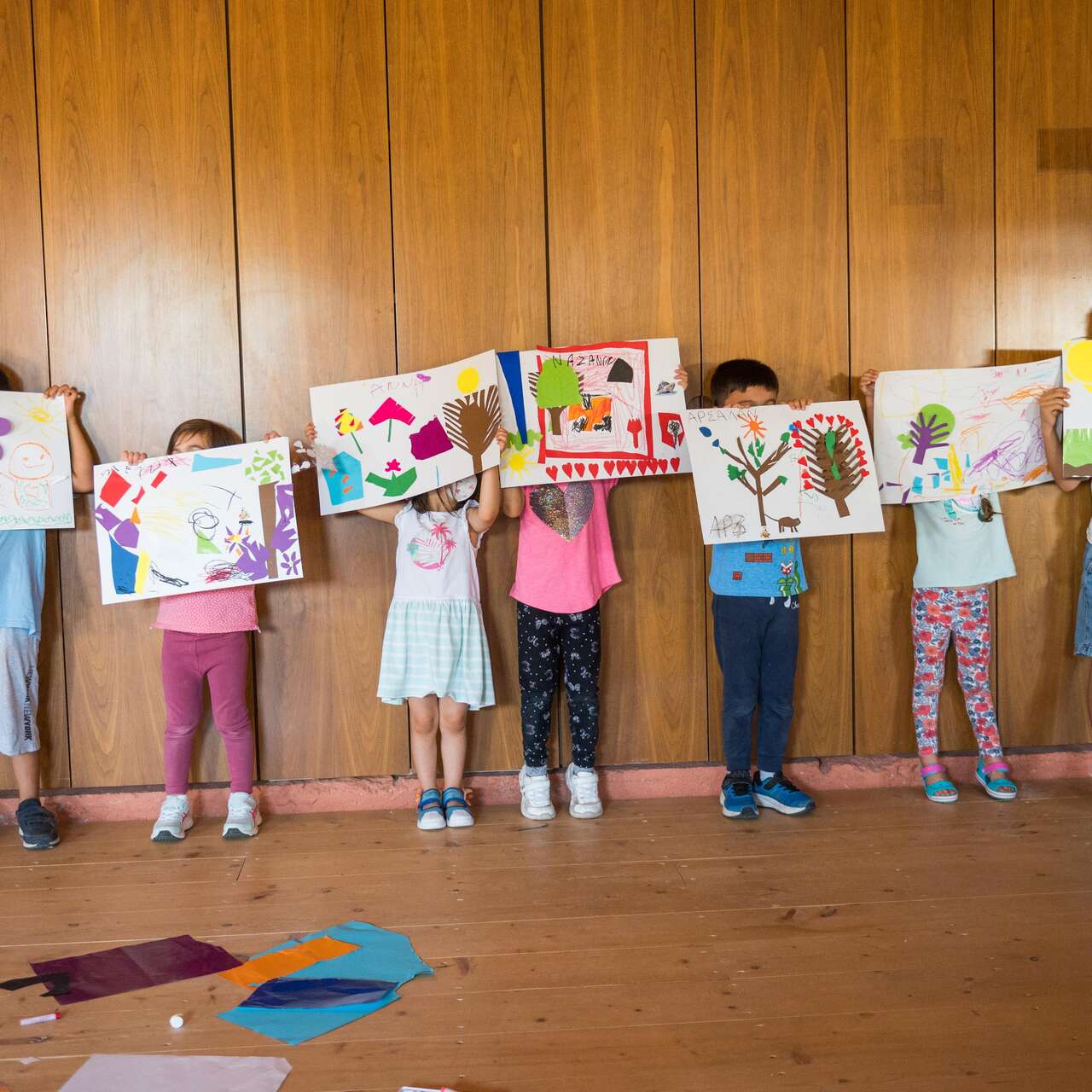 Children holding up their drawing over their faces