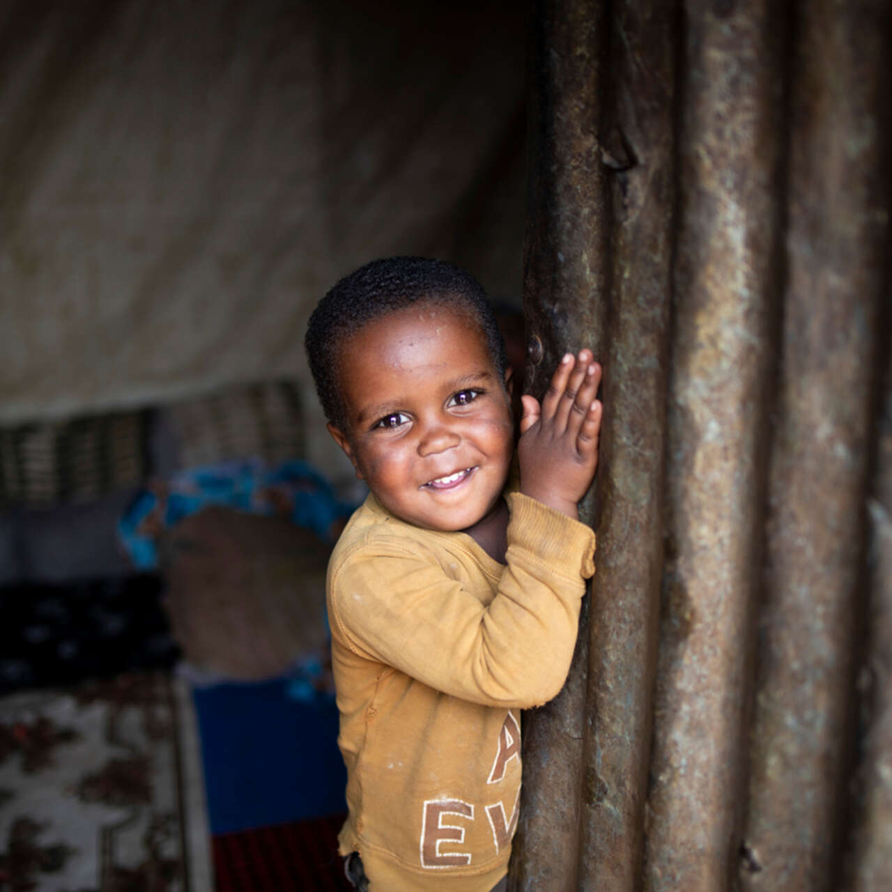 Kindesa (3) lächelt, als er die Tür seines Zuhauses im Geflüchtetenlager für Binnenvertriebene in Deder, Äthiopien, öffnet.