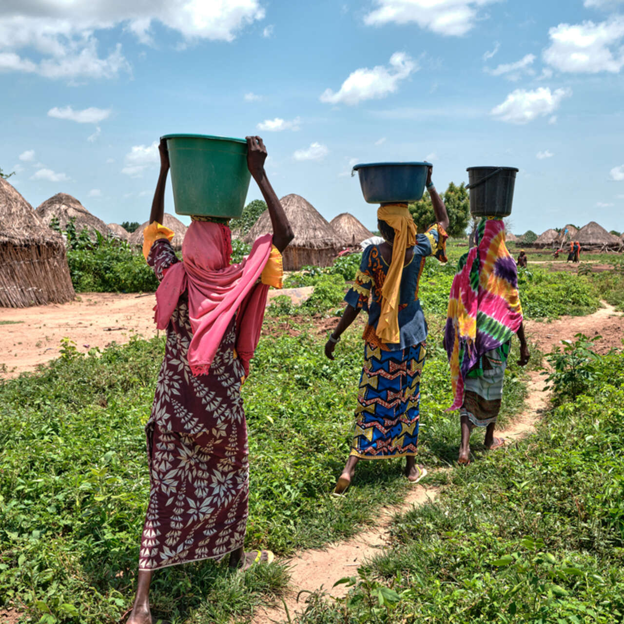 Tre kvinnor går på en stig och bär hinkar på sina huvuden.