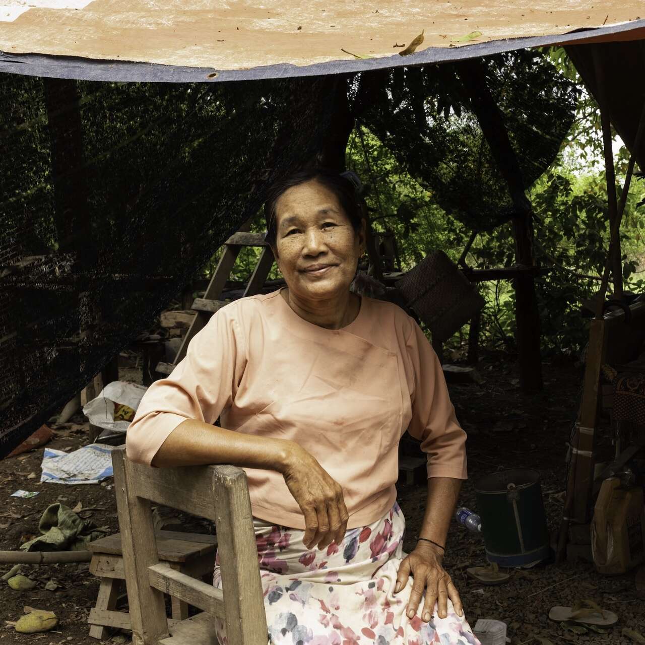 한 여성이 텐트 아래 앉아서 카메라를 바라보고 있습니다.