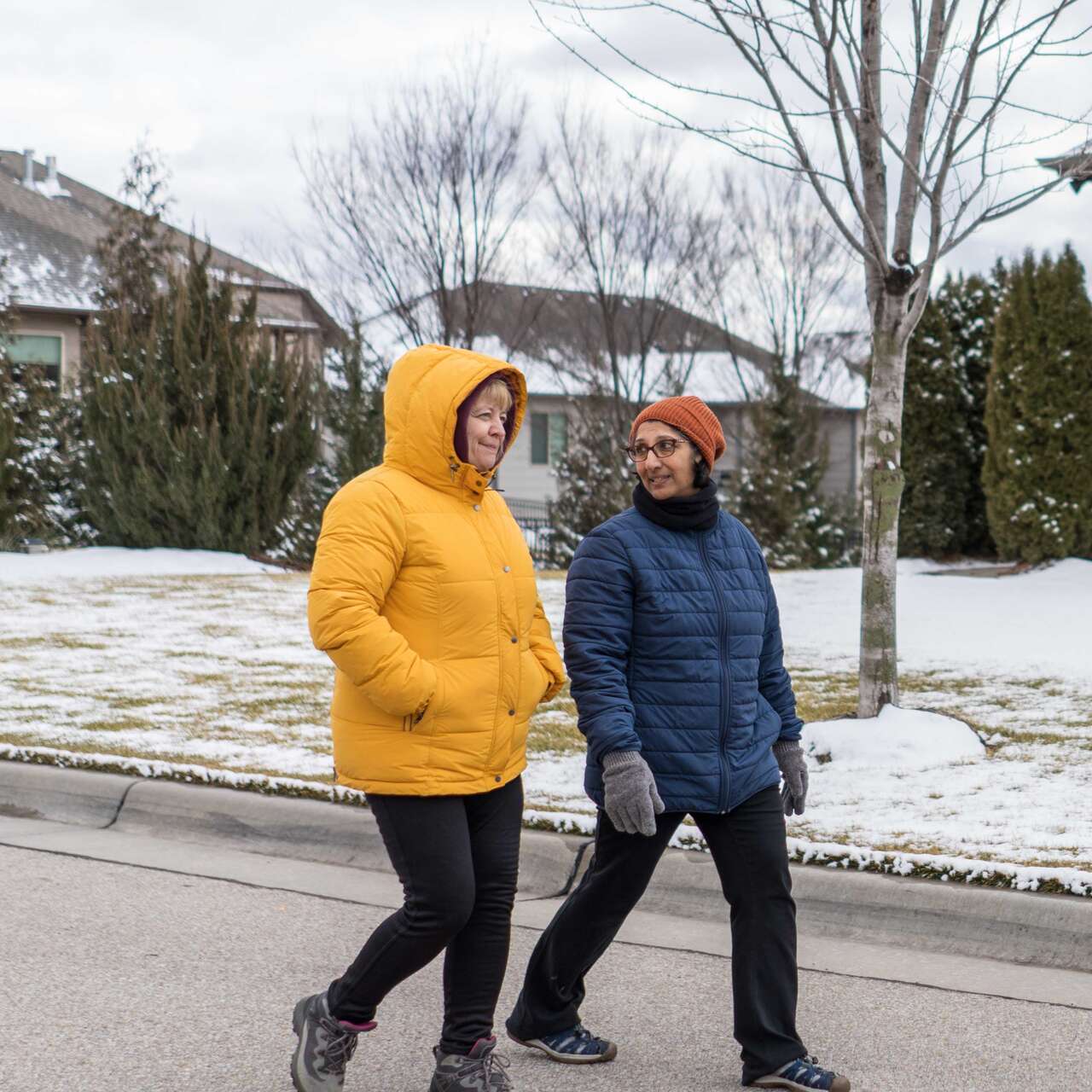Two women walk together through a residential neighborhood in winter.