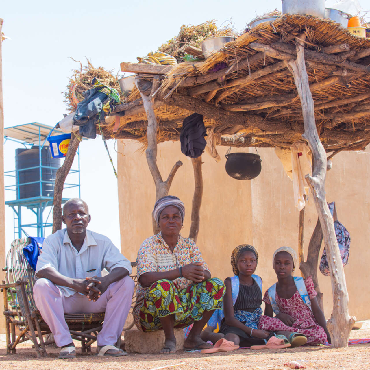 Bila Natama sitzt mit ihren Töchtern und ihrem Mann unter einem Unterstand vor ihrem Grundstück in Tibga, Burkina Faso 