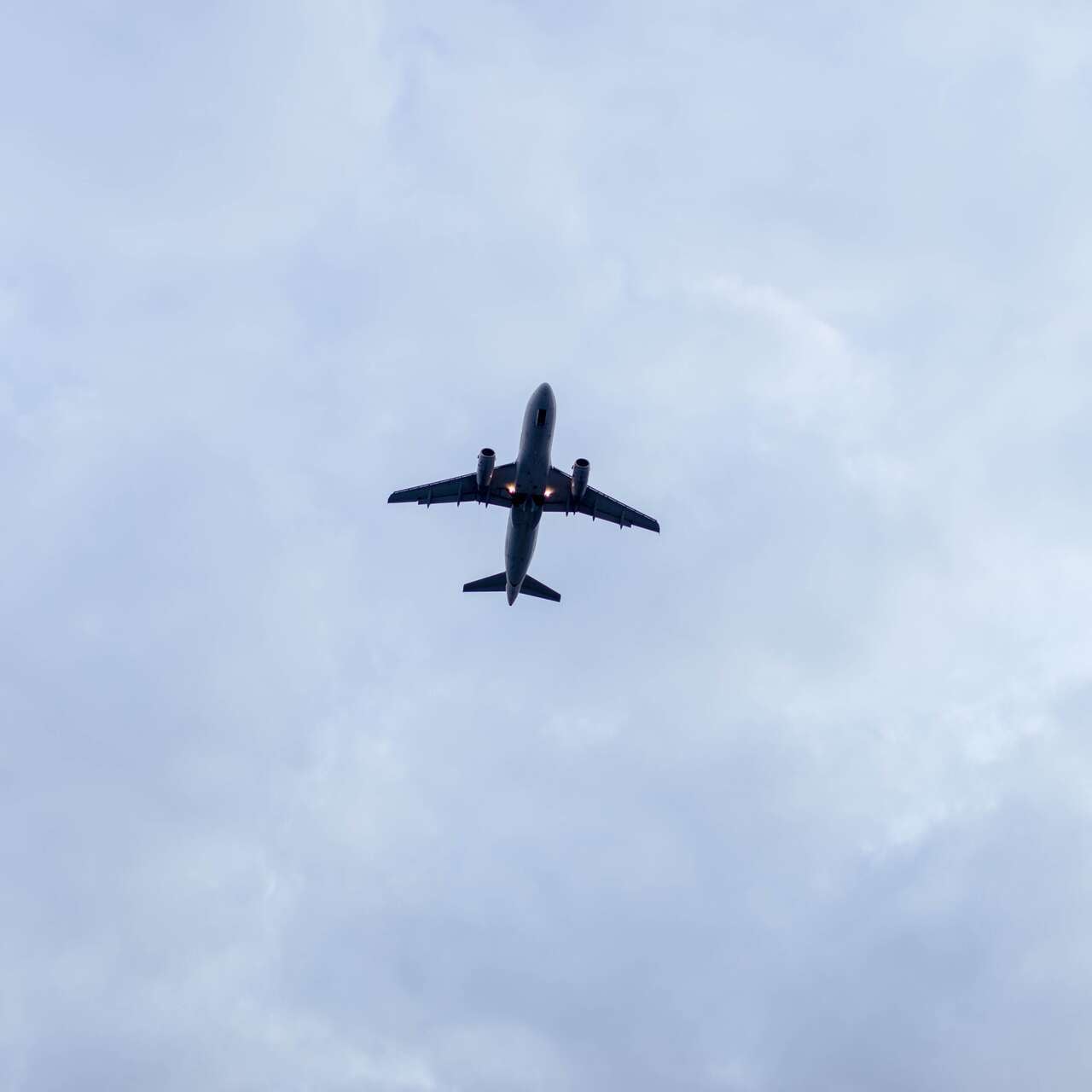An airplane flies overhead, against a cloudy sky.
