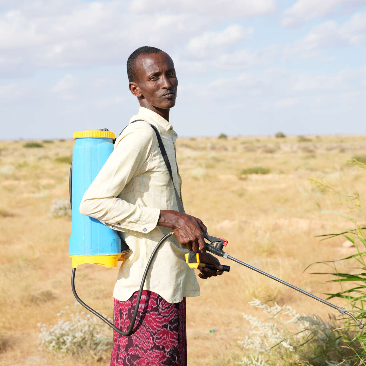 Man standing with pesticide spray in front of arid landscape
