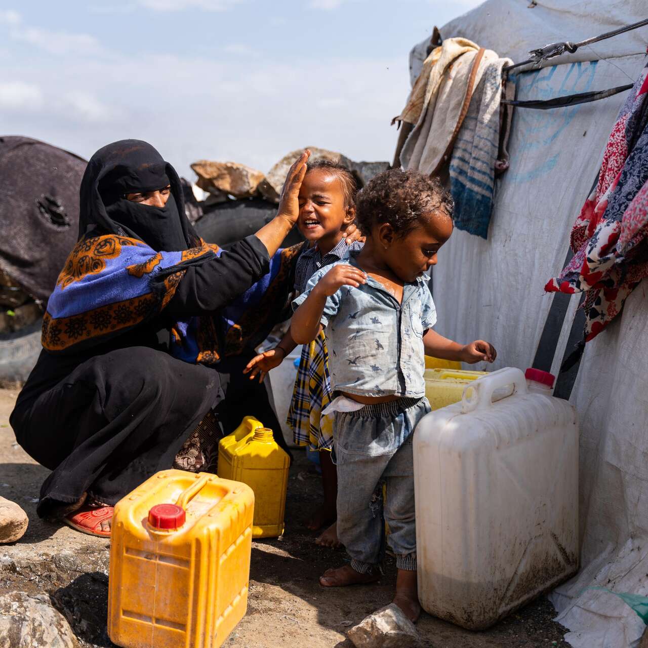 Asriya washing the face of her children in front of their tent.