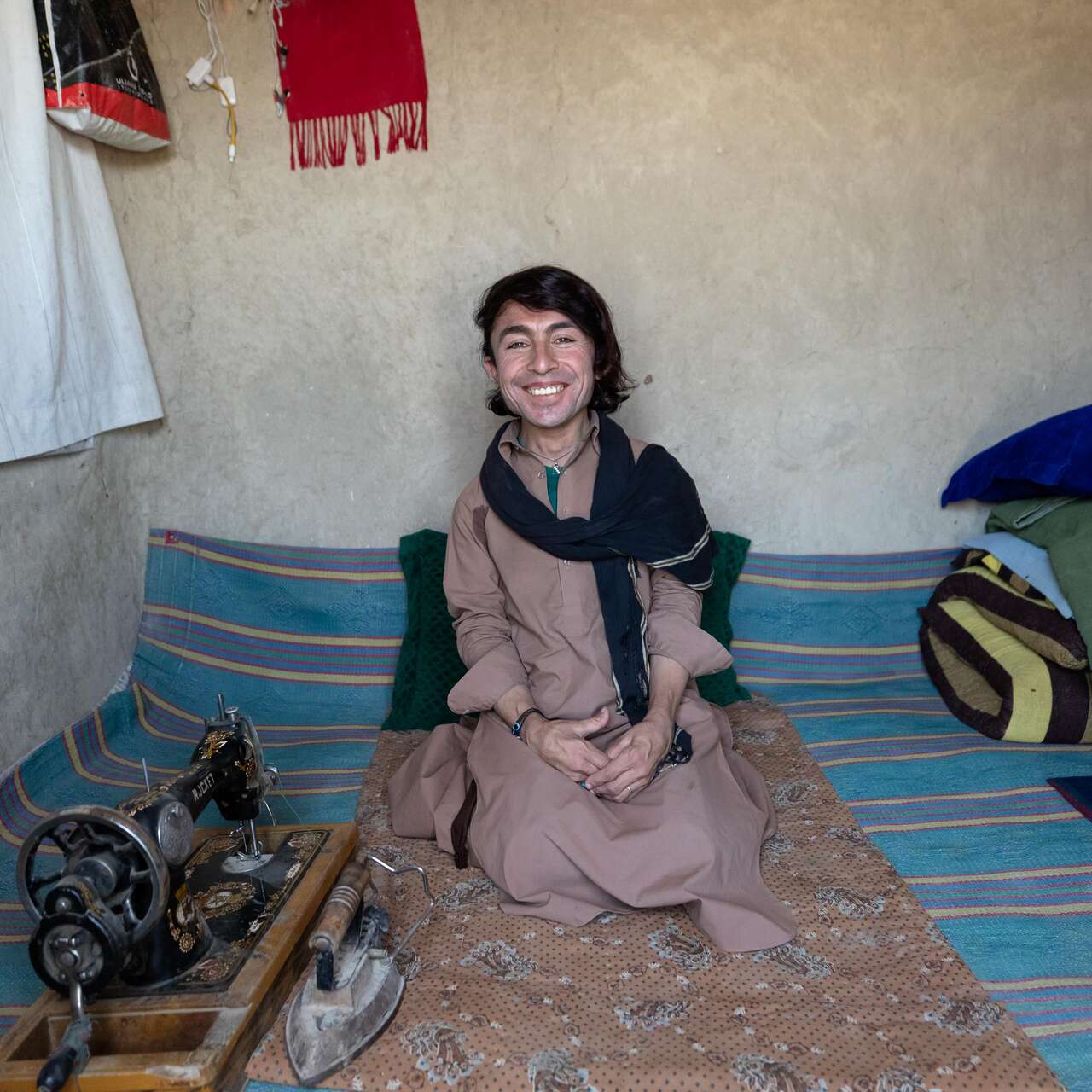 Darweza sits smiling at home beside his sewing machine.