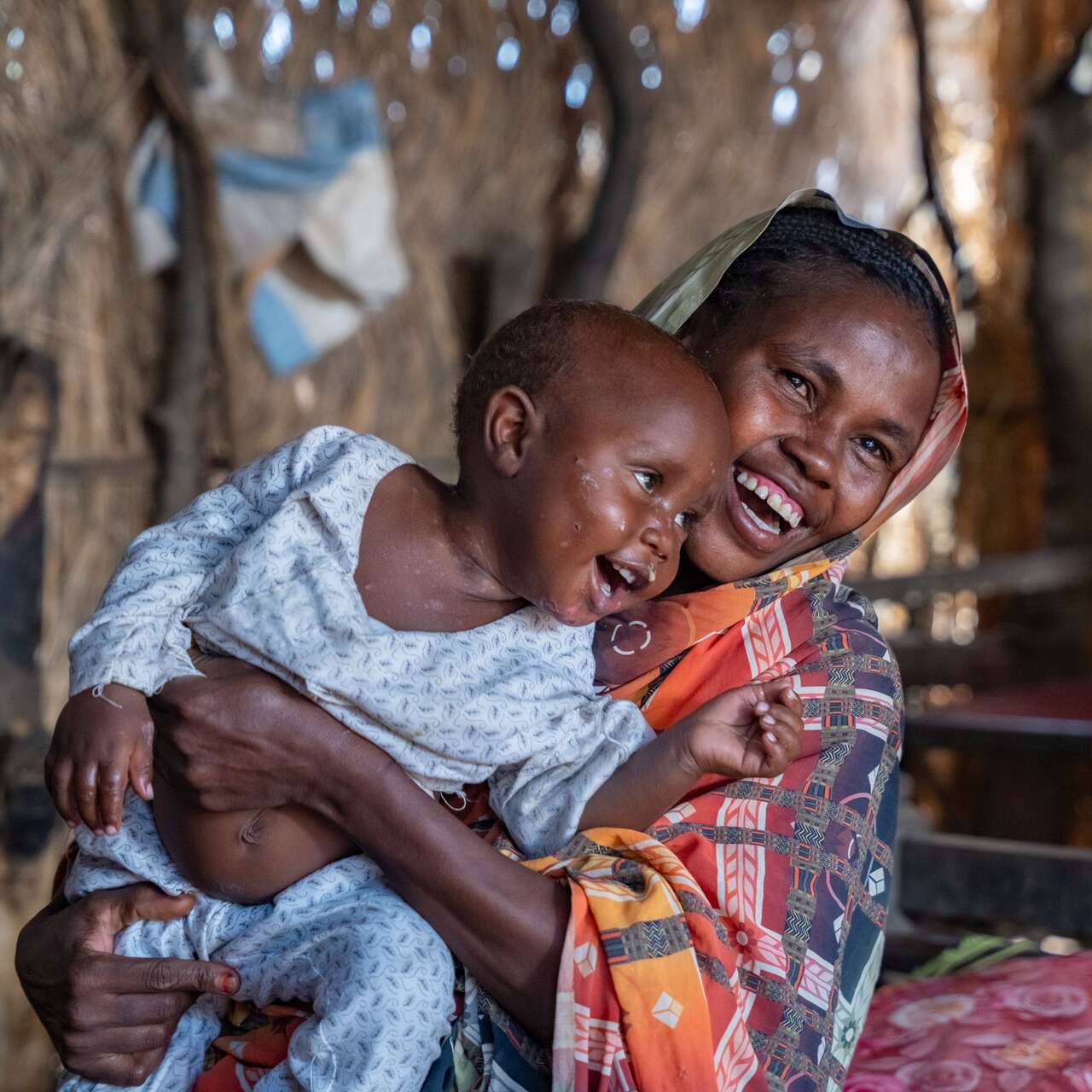 A mother holds her young child close as the two share a smile while playing.