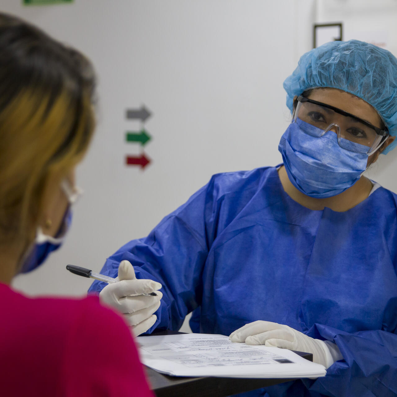 An IRC health worker wearing PPE to protect against COVID-19 holds a pen as she speaks with a patient to complete her paperwork.