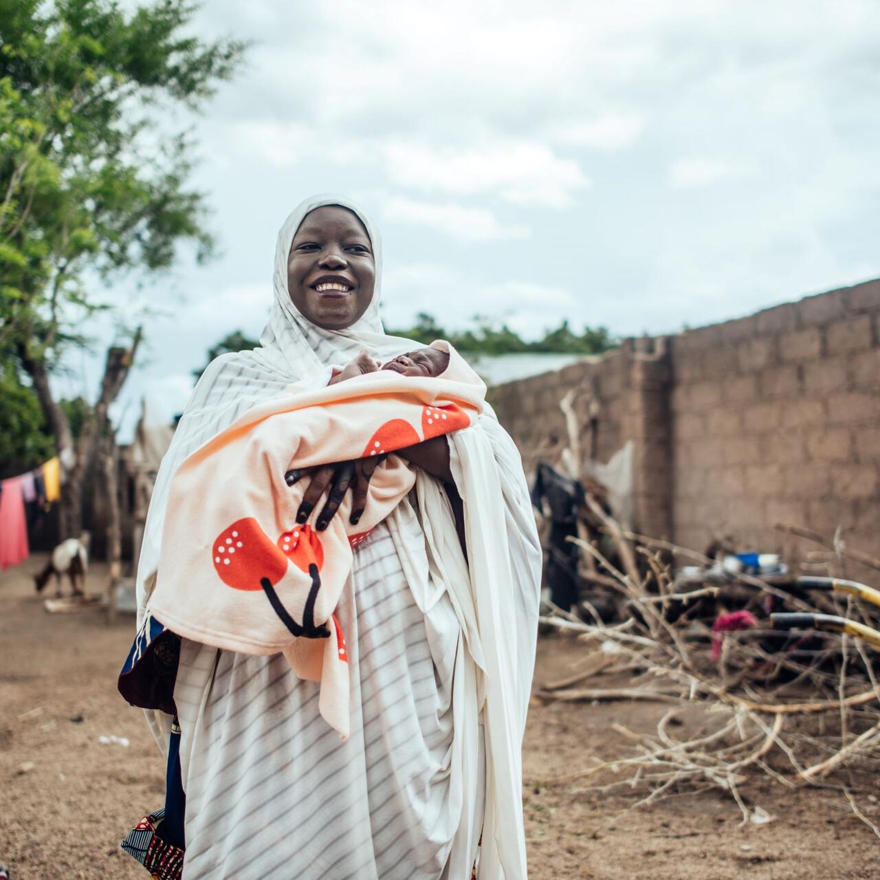 A Nigerian mother smiles and holds her baby who is wrapped in a blanket.