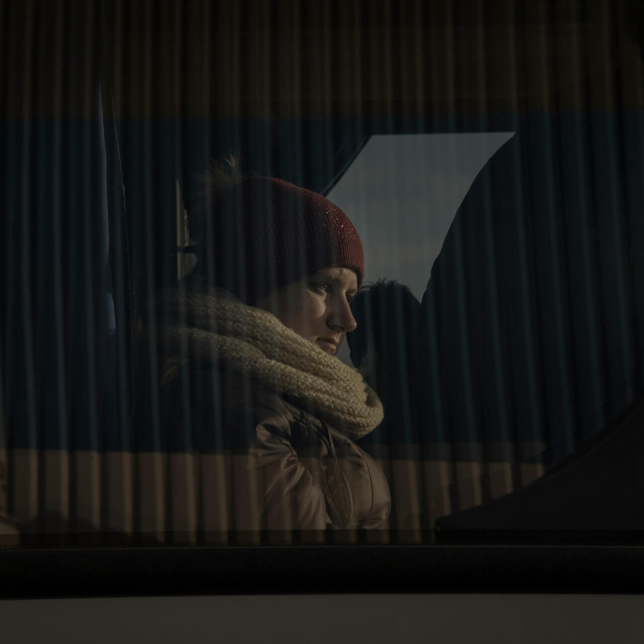 A woman sits in a bus wearing winter clothes and looks out the window. 