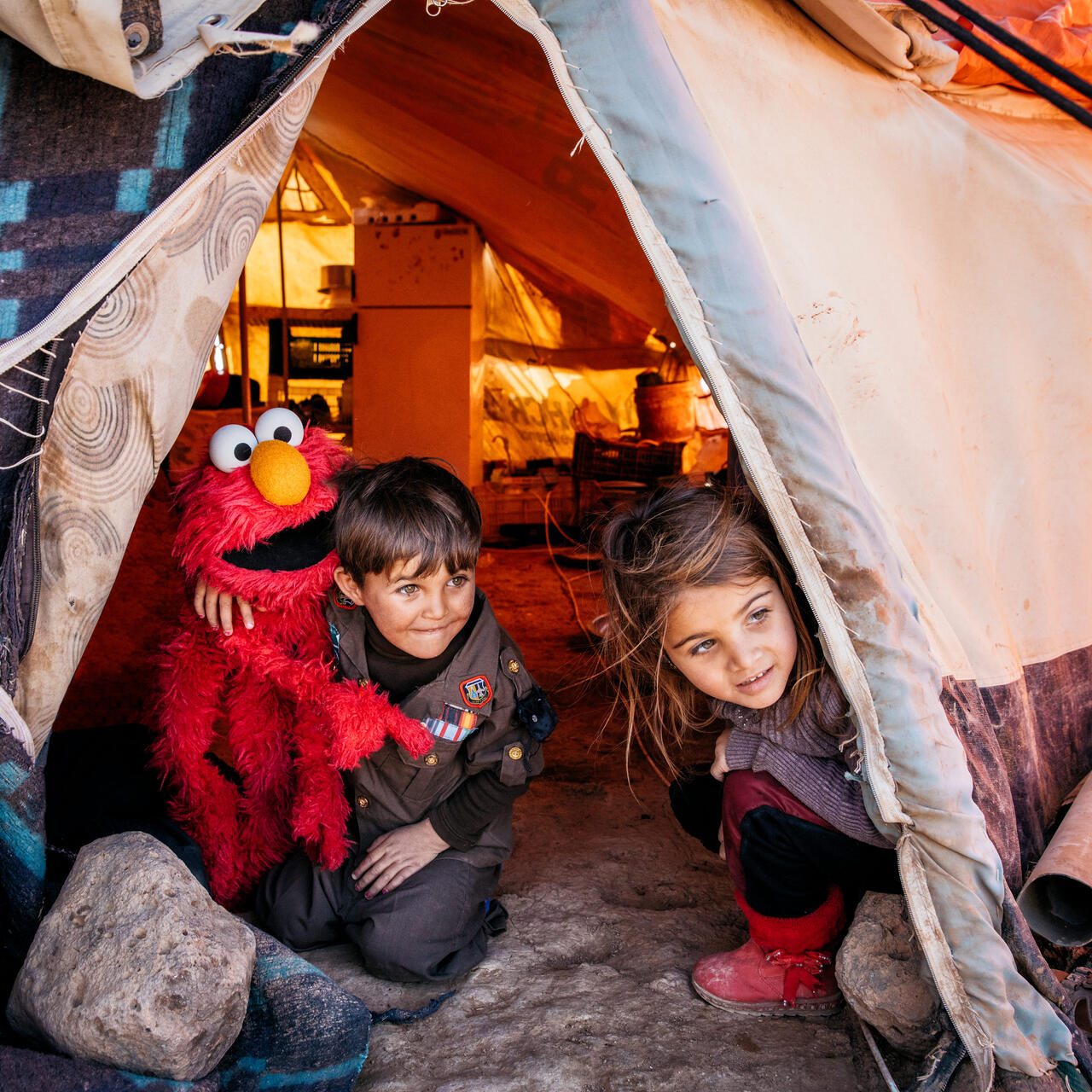 A young Syrian boy and girl with a Sesame Street Elmo puppet in their tent in a refugee camp in Jordan