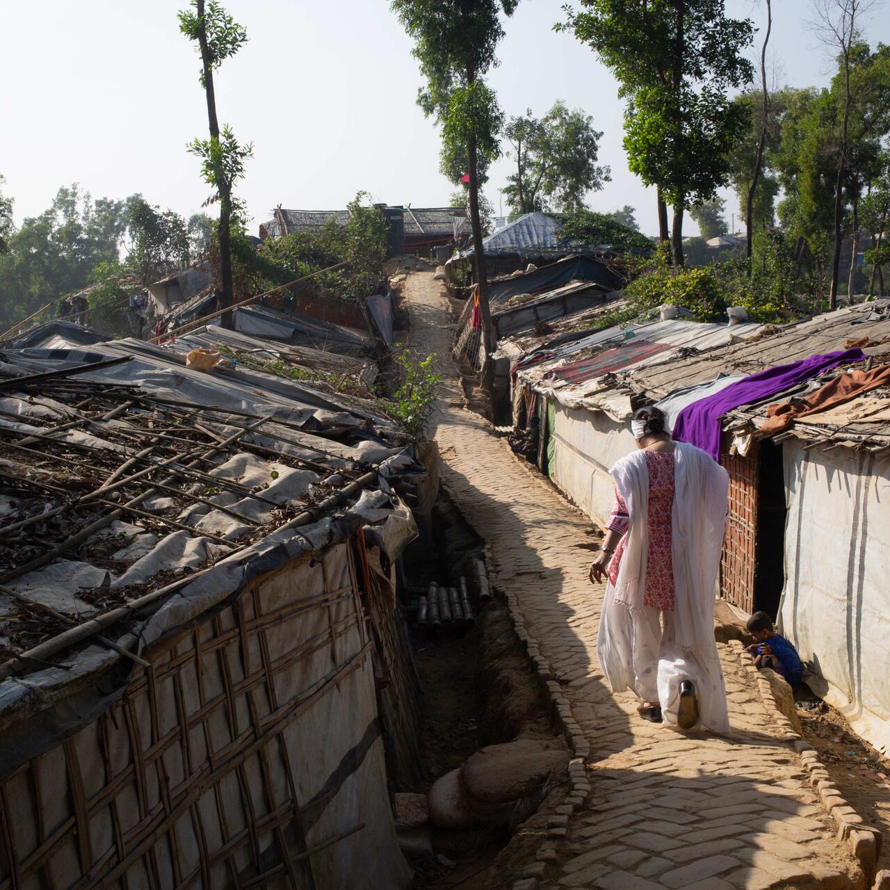 Razia Sultana walks in between a row of homes on a dust road