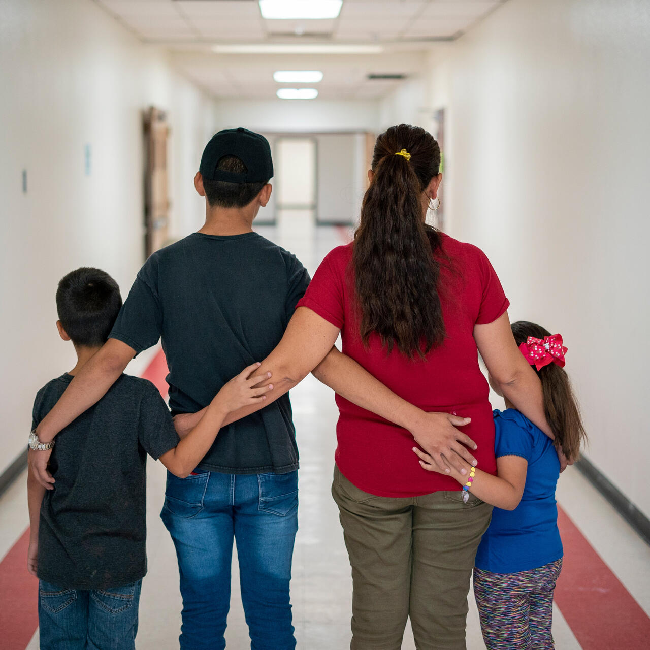 Luisa, an asylum seeker from Mexico, stands with with her children in Arizona after she was able to cross the US border. They are standing in a hallway with their backs to the camera, to protect their identities. 
