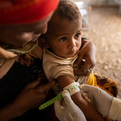 An IRC health care worker assesses a young child's health using a MUAC screening tape in Sudan to determine malnutrition.
