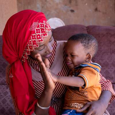 A mother holds her son, clapping hands together in a health center in Burkina Faso.