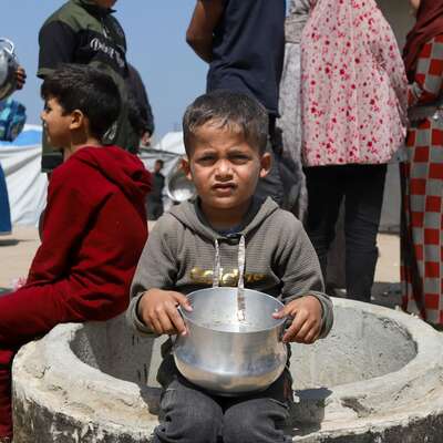 A Gazan child sits with an empty bowl waiting for aid