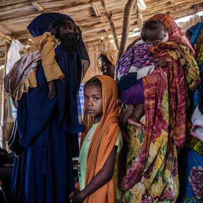 En liten flicka står i en kö i Sudan, bland kvinnor som håller i sina spädbarn. 