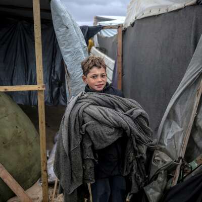 Boy standing by a tent wearing a warm blanket