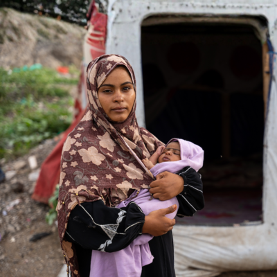 En ung kvinna, Ruwaidah, håller sitt nyfödda barn Mortada framför ett tält på ett flyktingläger i Jemen.