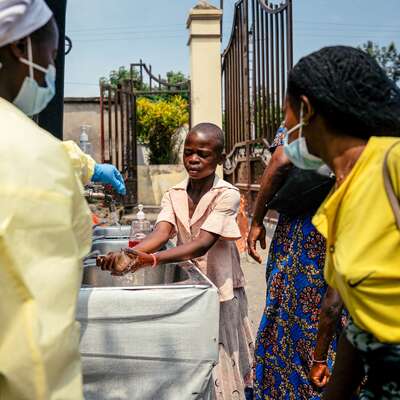 A young girl washes her hands before entering Kyeshero Hospital at a checkpoint for hand washing and temperature screening for all visitors and patients