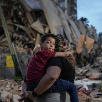 A person carries a child in front of a pile of rubble and destroyed buildings after an earthquake in Venezuela.