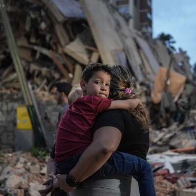A person carries a child in front of a pile of rubble and destroyed buildings after an earthquake in Venezuela.