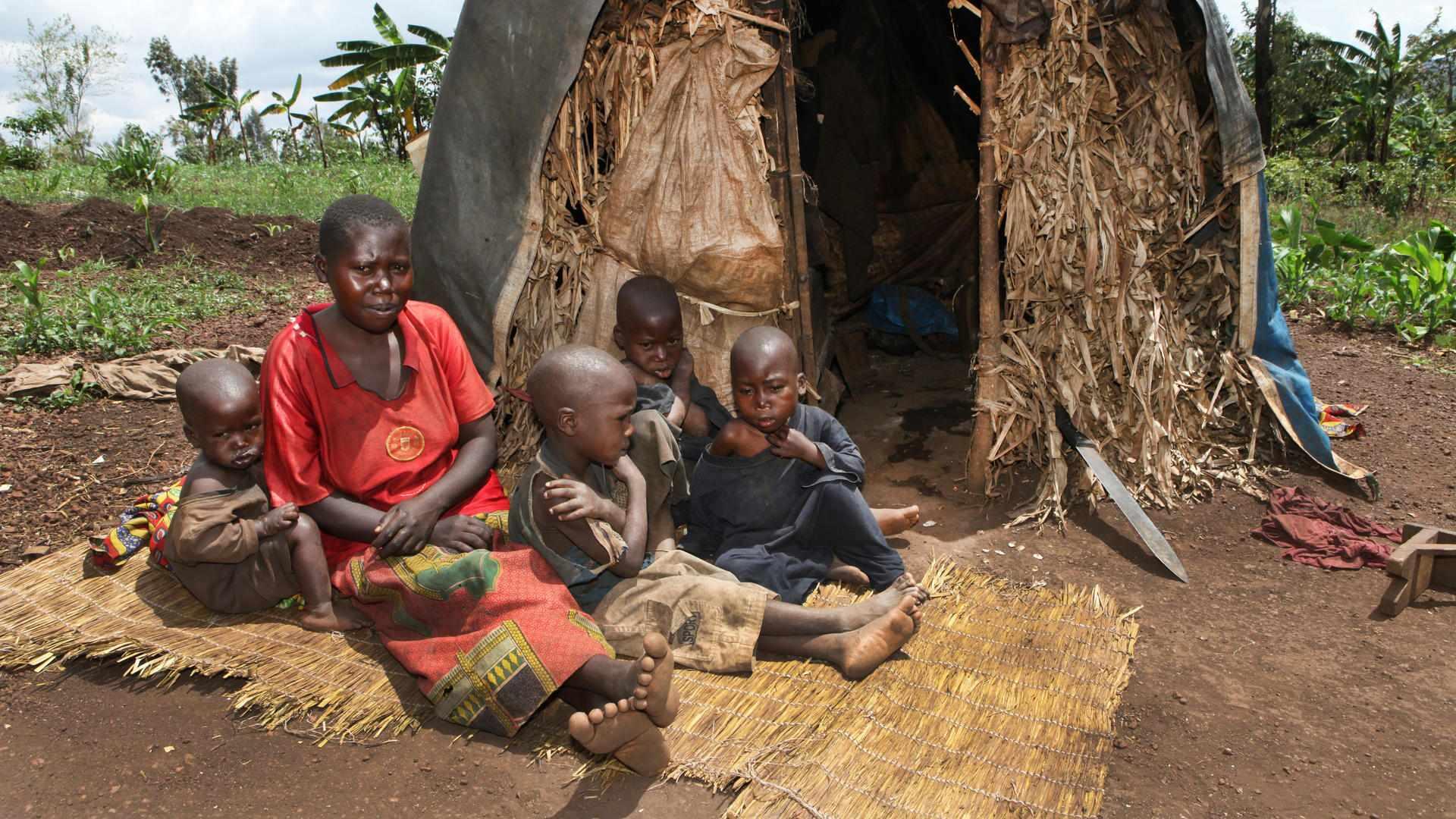 Eine Mutter sitzt mit ihren Kindern vor einer einfachen Hütte aus Holz