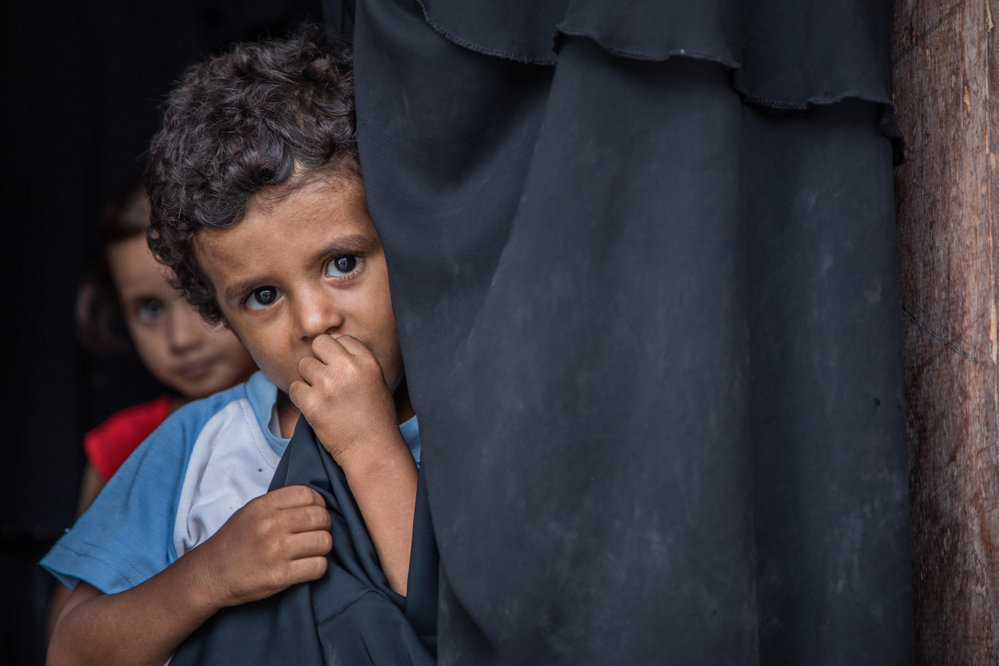 A young boy hiding behind a curtain