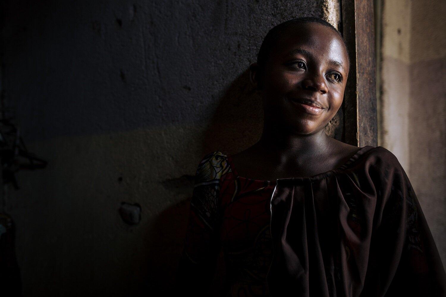 A women is smiling and leaning against a wall