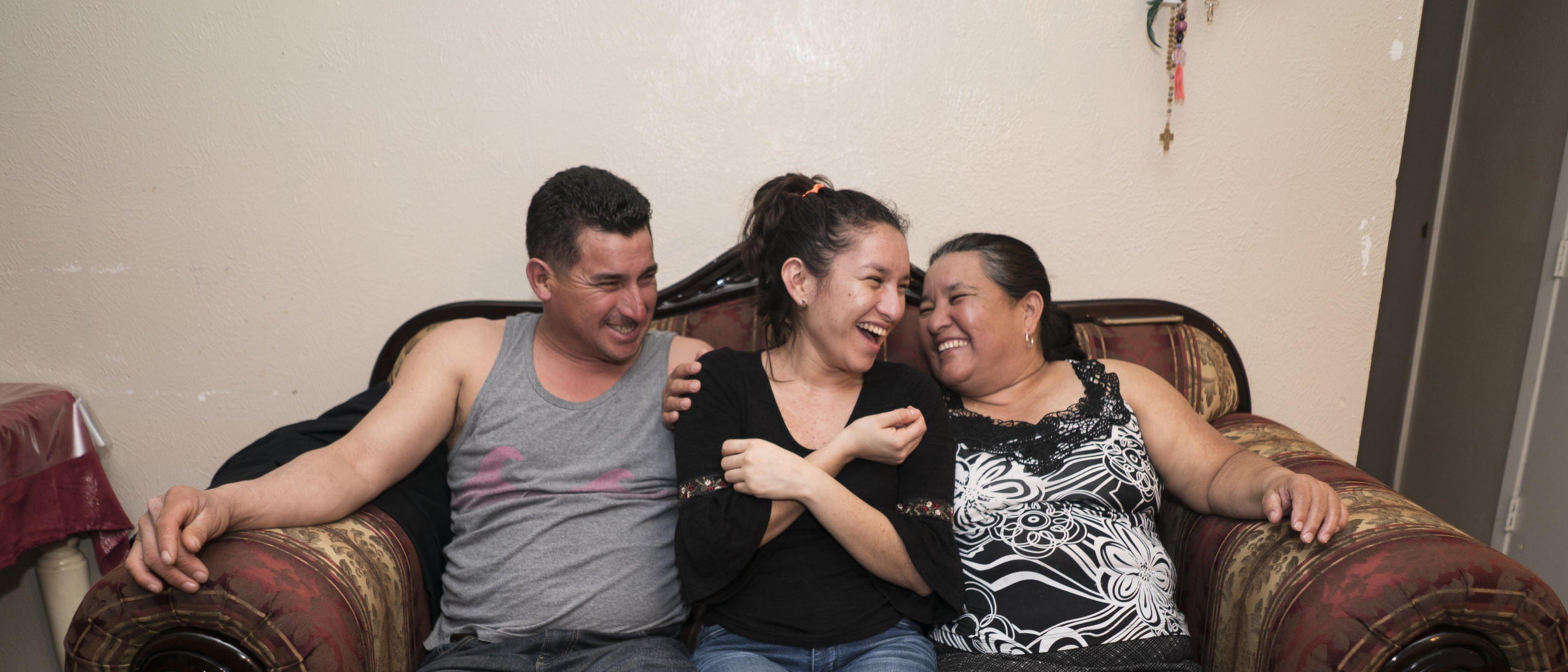three laughing people sitting on a sofa