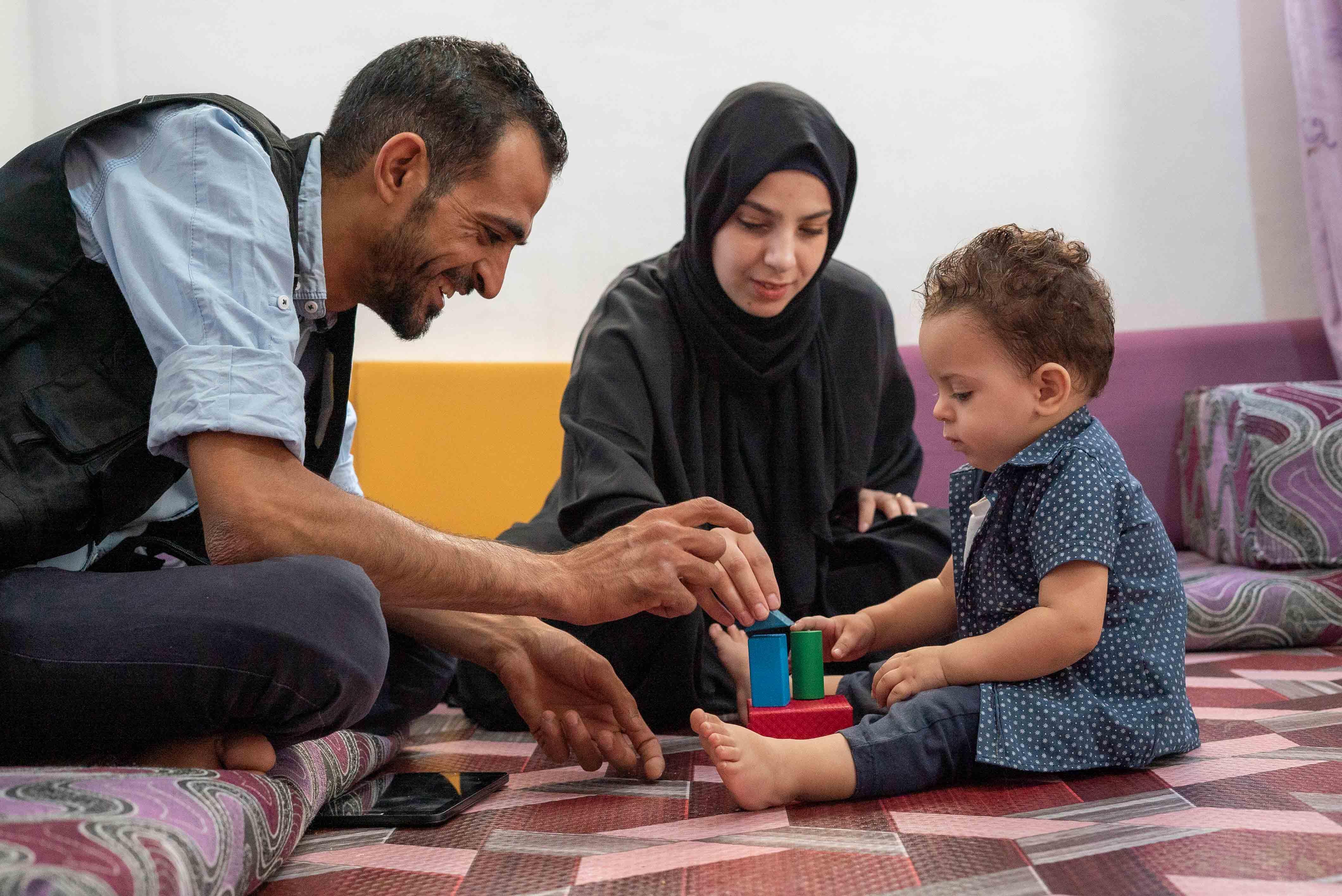 Anas, ein IRC-Freiwilliger, stärkt Familien in Jordanien und spielt mit einem Kleinkind und der Mutter.