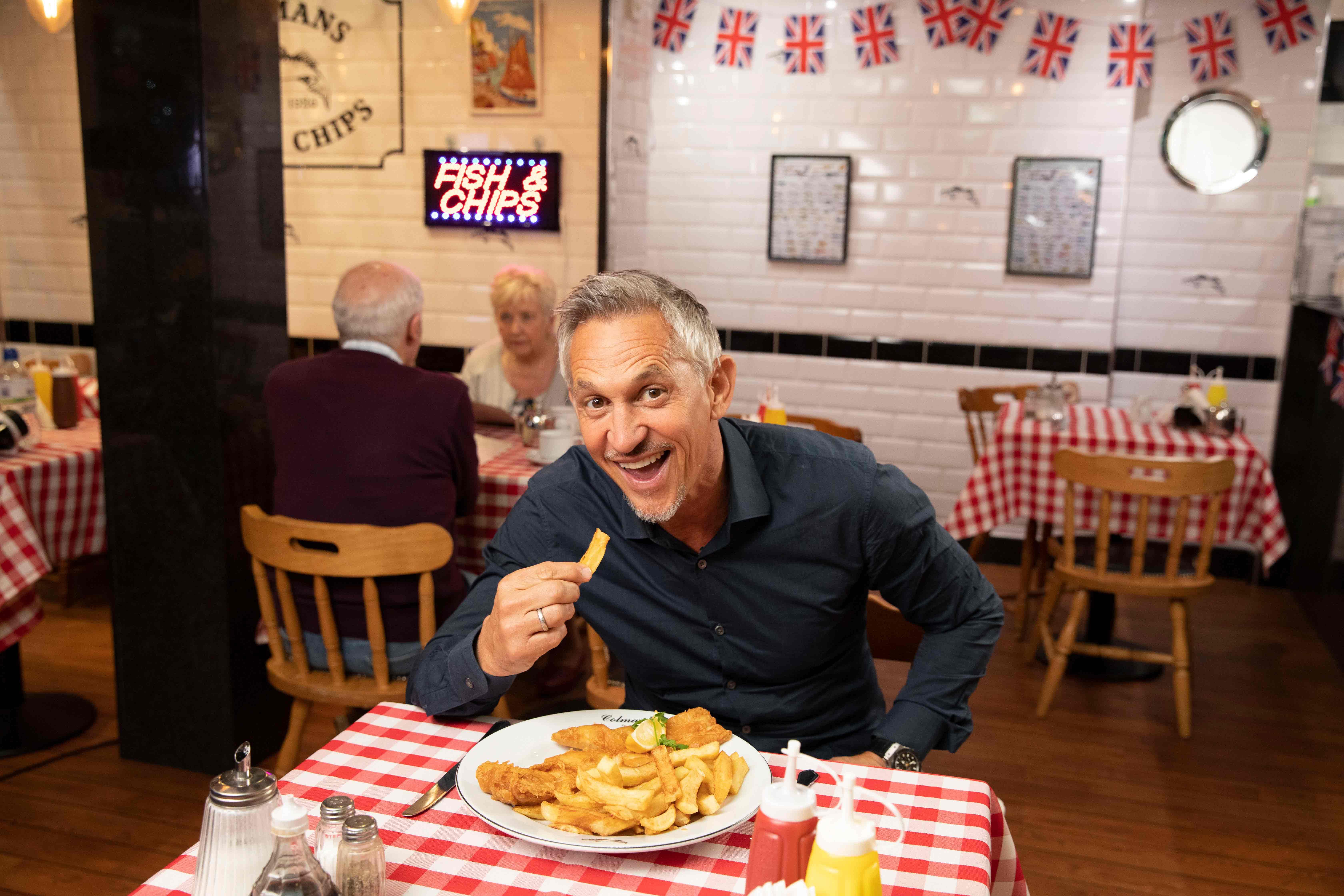 Gary Lineker sitzt an einem Tisch und isst Fish & Chips.