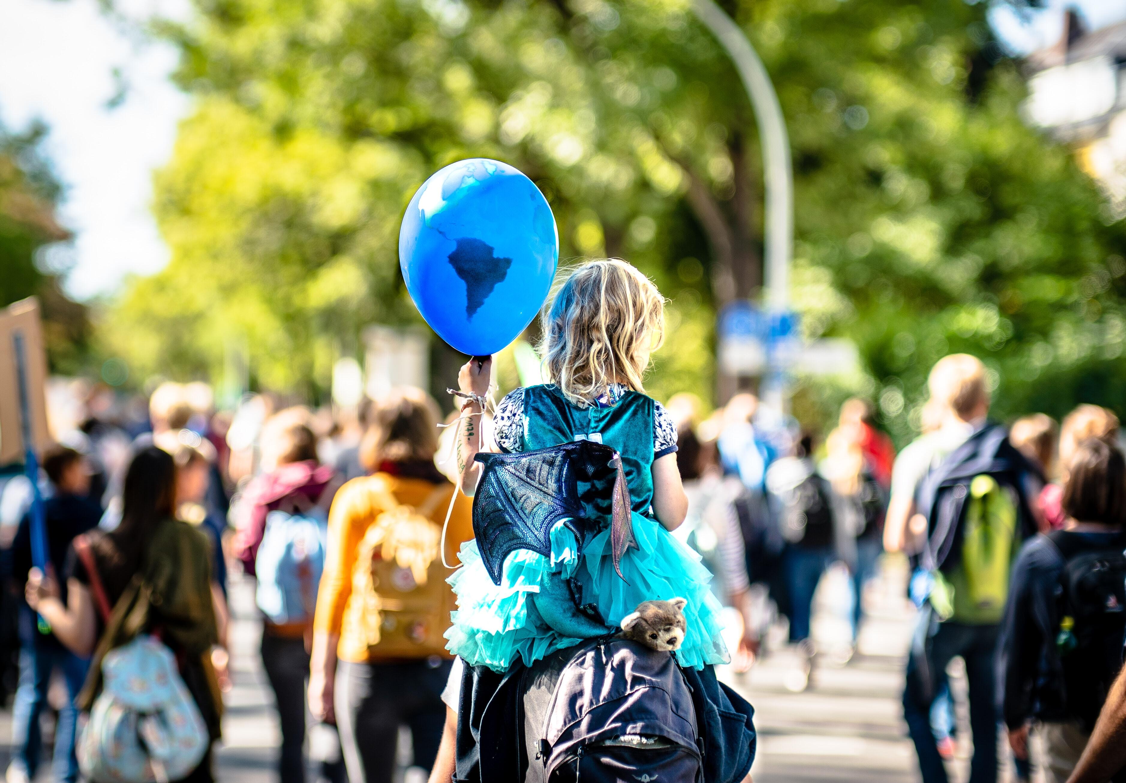 Inmitten eines Protests hält ein Kind einen Luftballon mit einer Weltkarte hoch.