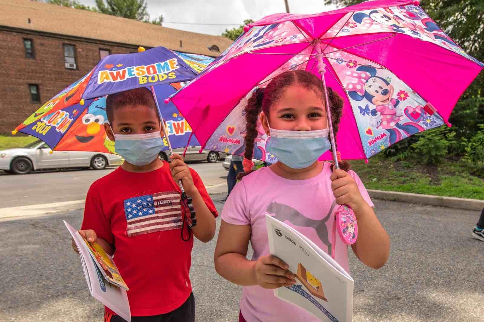 Children in masks with colourful umbrellas during COVID-19