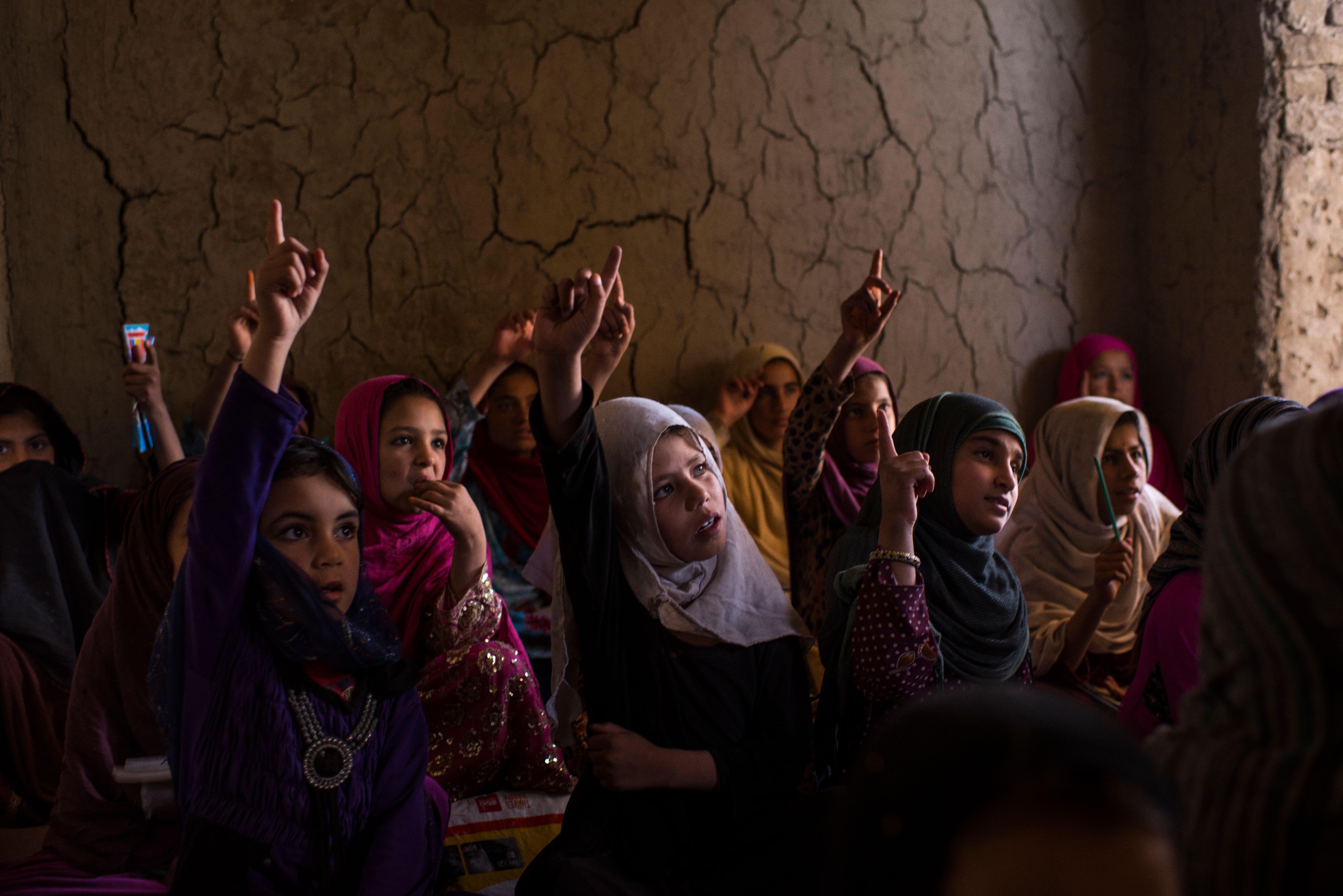 Eine Gruppe von Mädchen in Afghanistan sitzt im Unterricht. Die Mädchen haben ihr Hand erhoben und beteiligen sich an der Schul-stunde