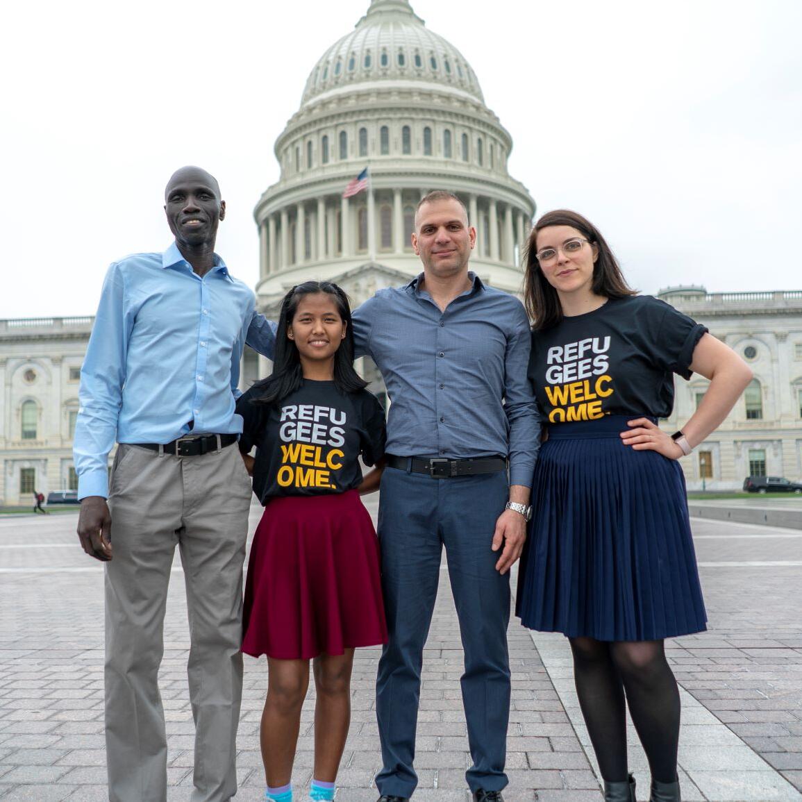 Members of the IRC's Refugee Voices program, two men and two women, stand in front of the U.S. Capitol. The women are wearing shirts that say Refugees Welcome. 