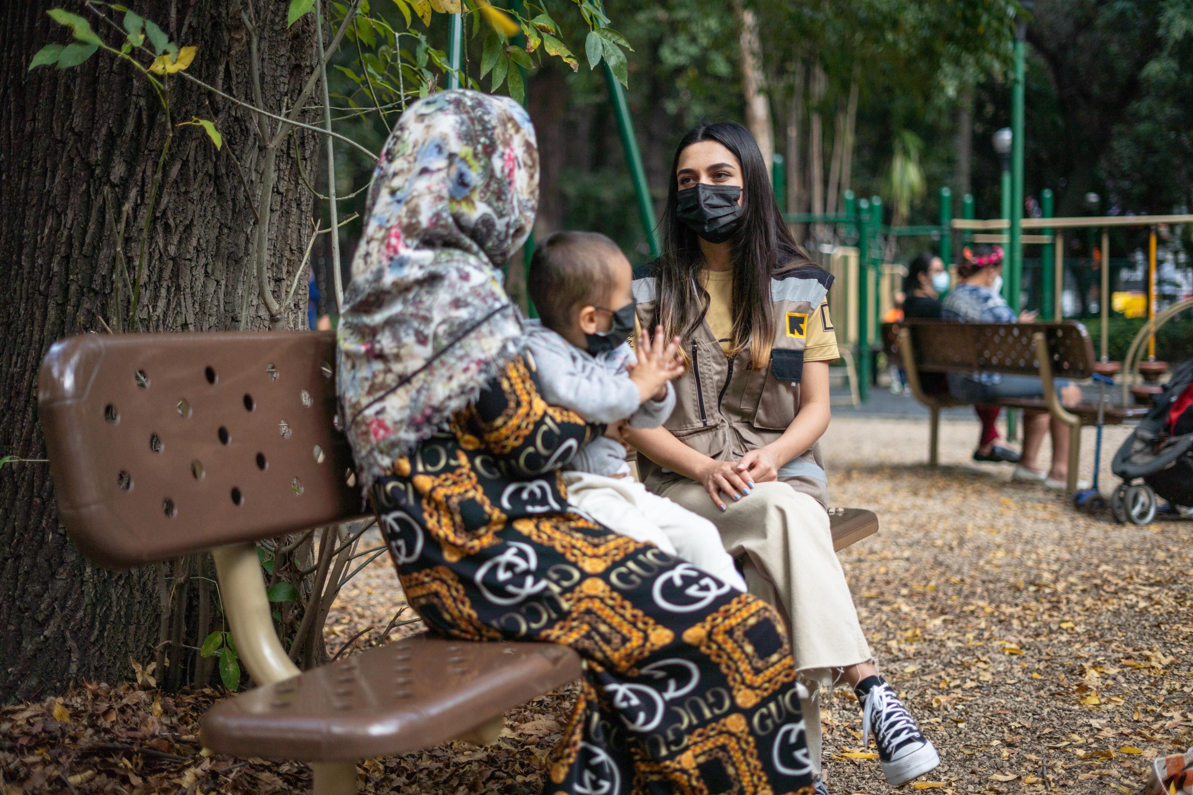 한여성IRC 통역관이멕시코시티놀이터의공원벤치에앉아아기를안고있는아프간어머니와이야기하고있습니다.