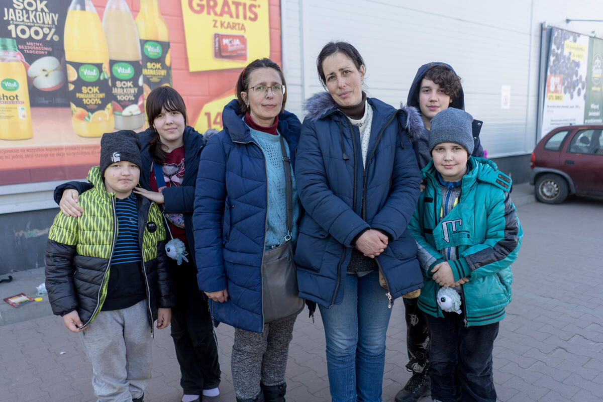 Two sisters stand together in a parklng lot. Each sister has her own two kids with her.