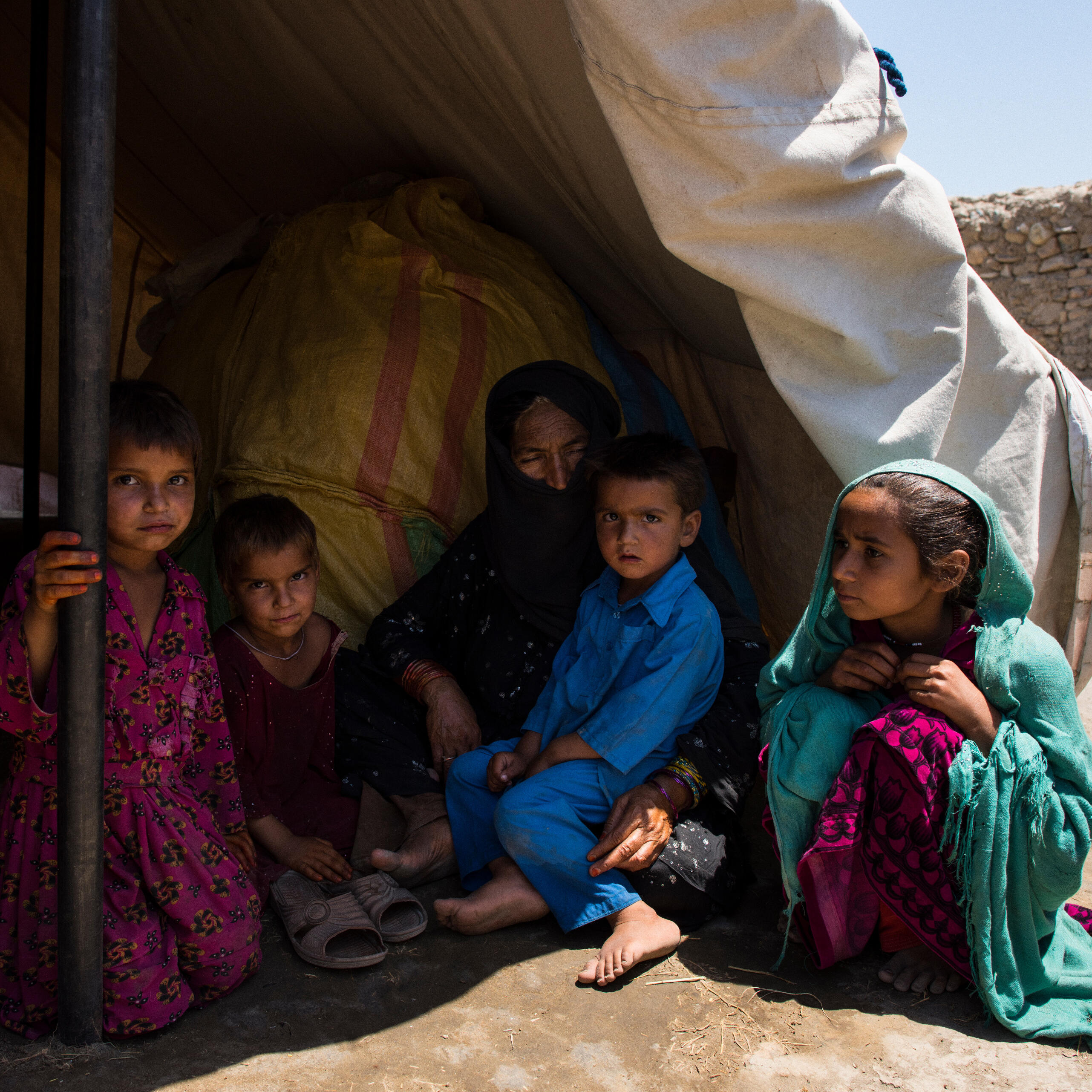 An Afghan family sits in the shade of an open tent