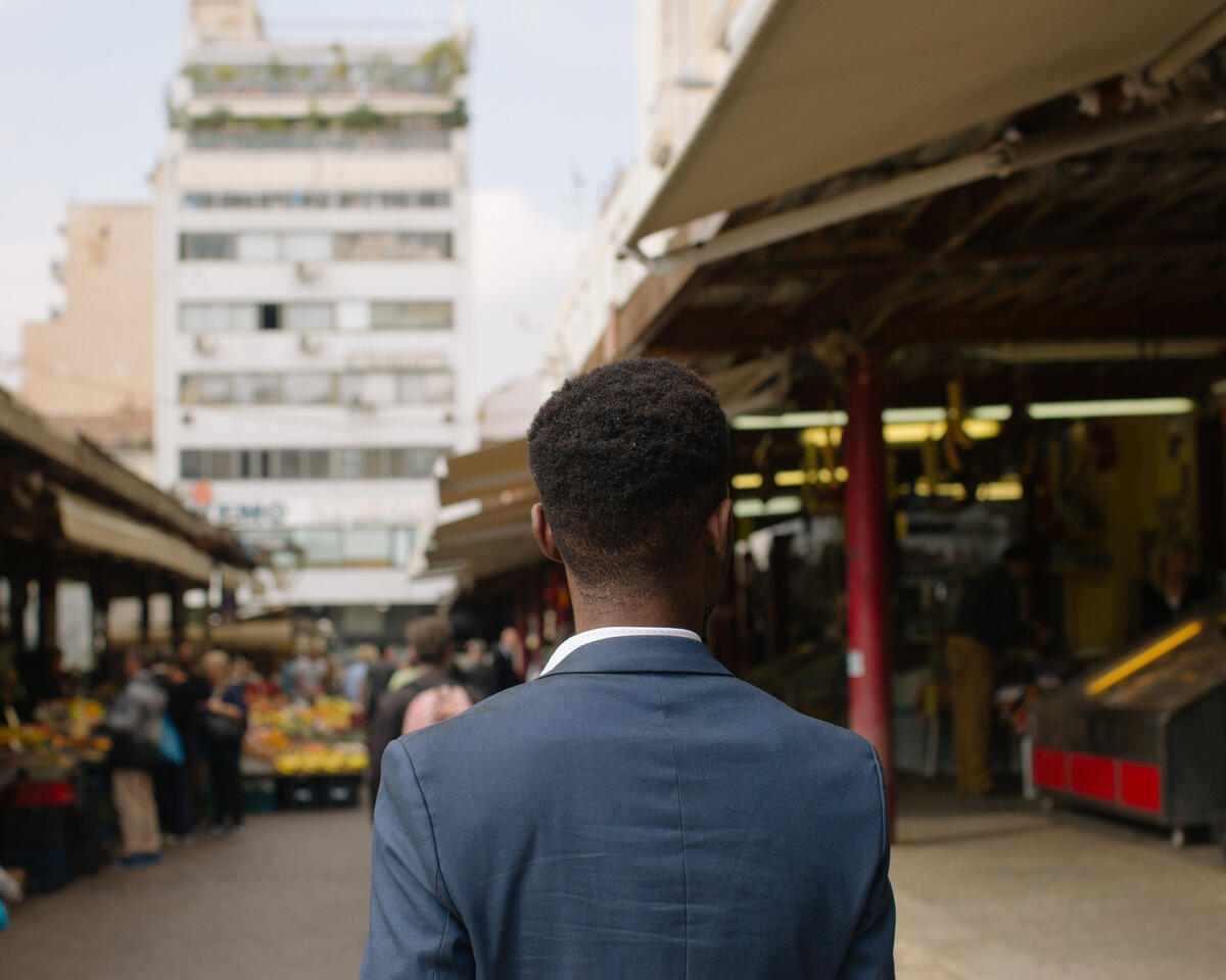 Moussa, a refugee from Ivory Coast, walks through a food market in Athens