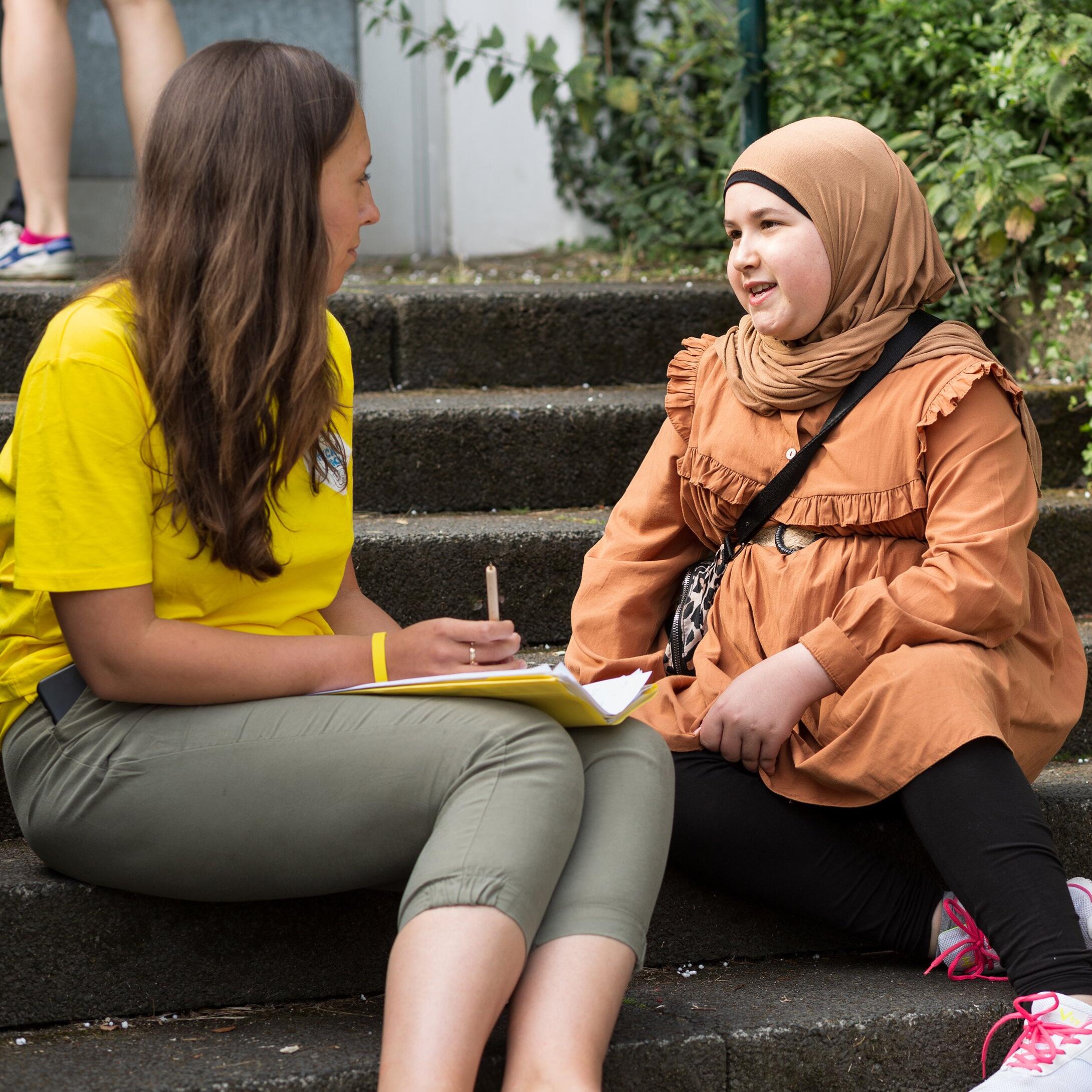 Teacher Jeannine and student Rawan in front of the school building talking.