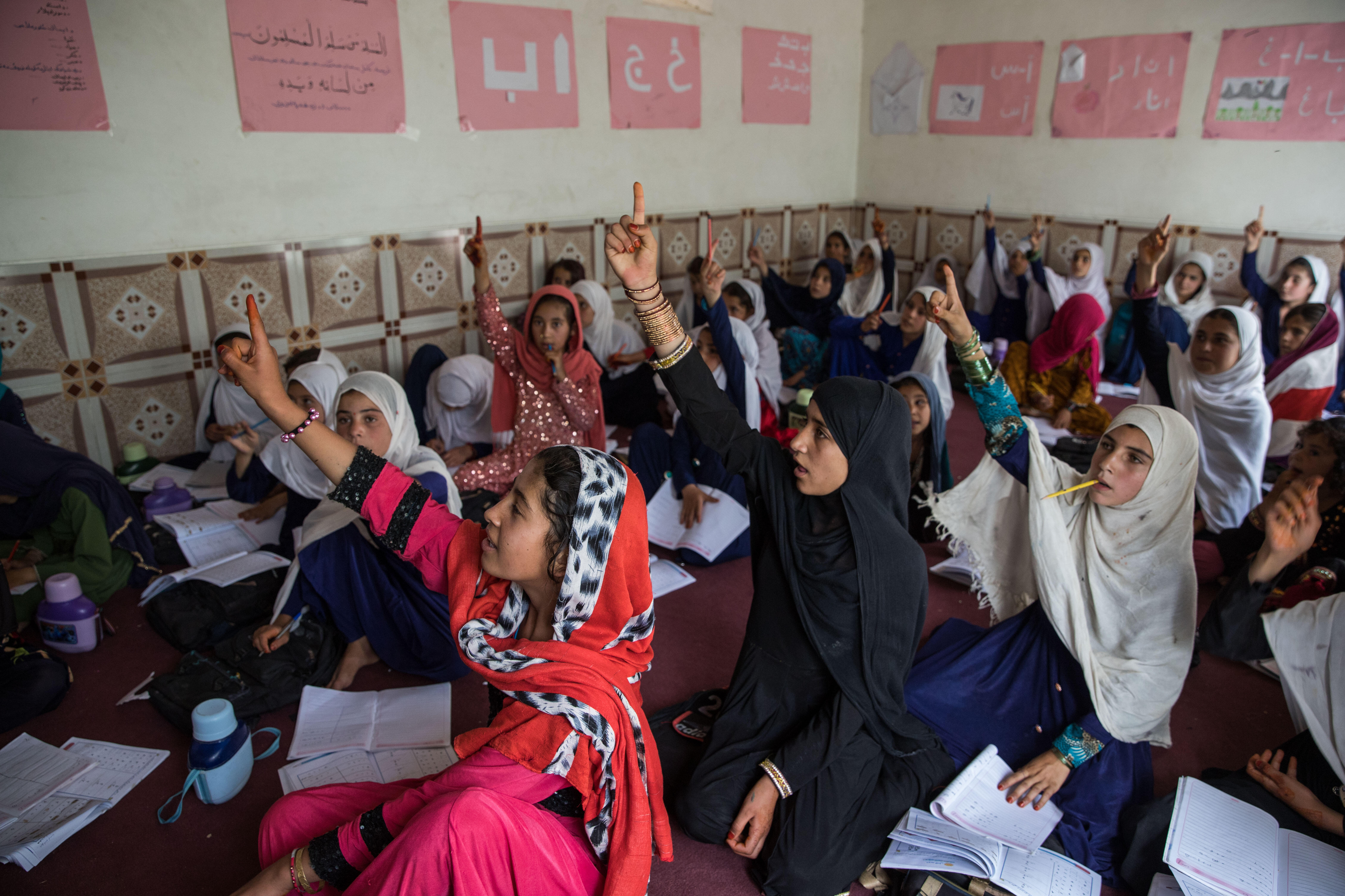 Girls sitting on the floor raise their hands in an IRC community education program in Afghanistan