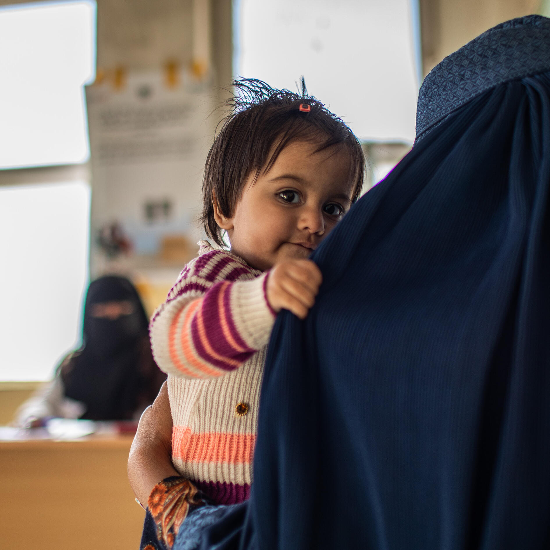 A young girl looks over her mothers shoulder at an IRC clinic in Afghanistan.