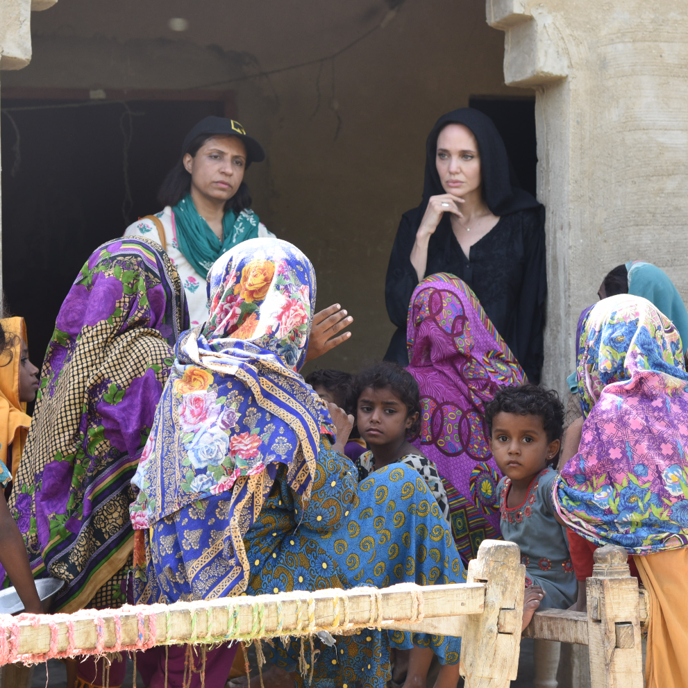 Angelina Jolie visits with women affected by flooding and Pakistan. A few girls look on at the forefront of the picture.