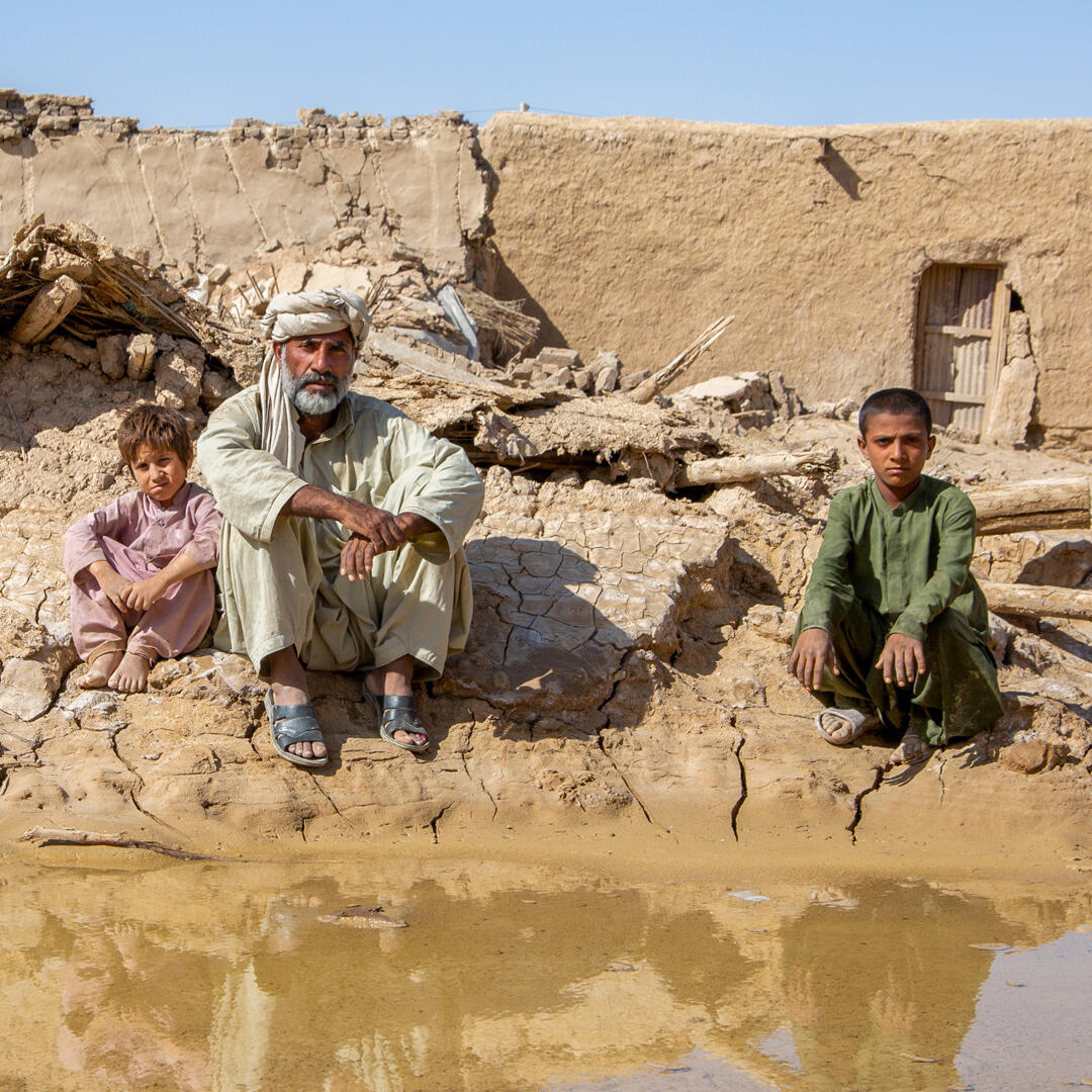 Grandfather and his grandchildren sitting over what remains of their home after severe floods in Pakistan.