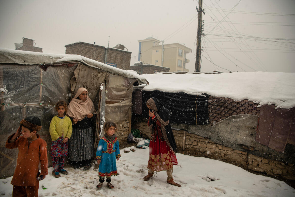 An Afghan family huddles in the snow outside their makeshift house