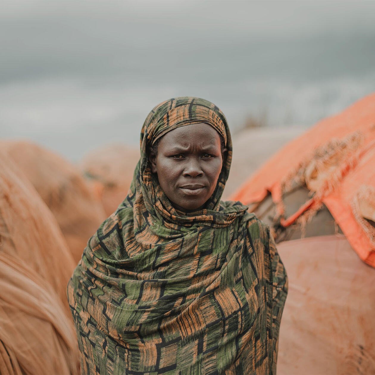Portrait of a woman standing in front of a series of huts in the Somali desert.