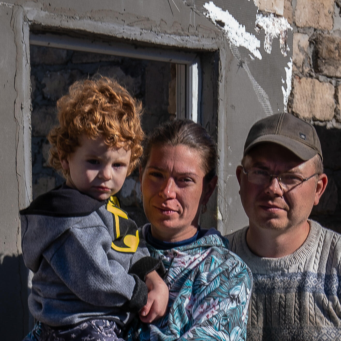 A family of three stand in front of their missile-destroyed house in Ukraine.